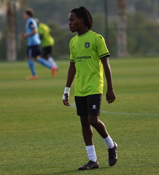 Football Academy player in green kit walking on football pitch